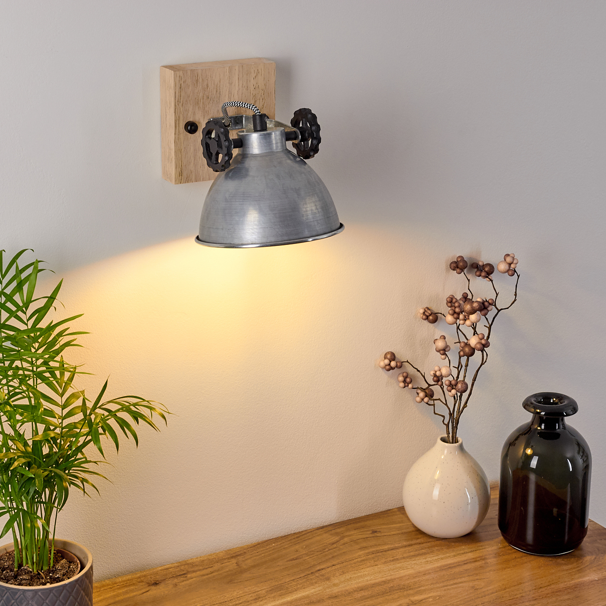 Wandlampe, die Licht auf einen Tisch mit Pflanzen und Vasen wirft und eine gemütliche, beleuchtete Umgebung schafft.