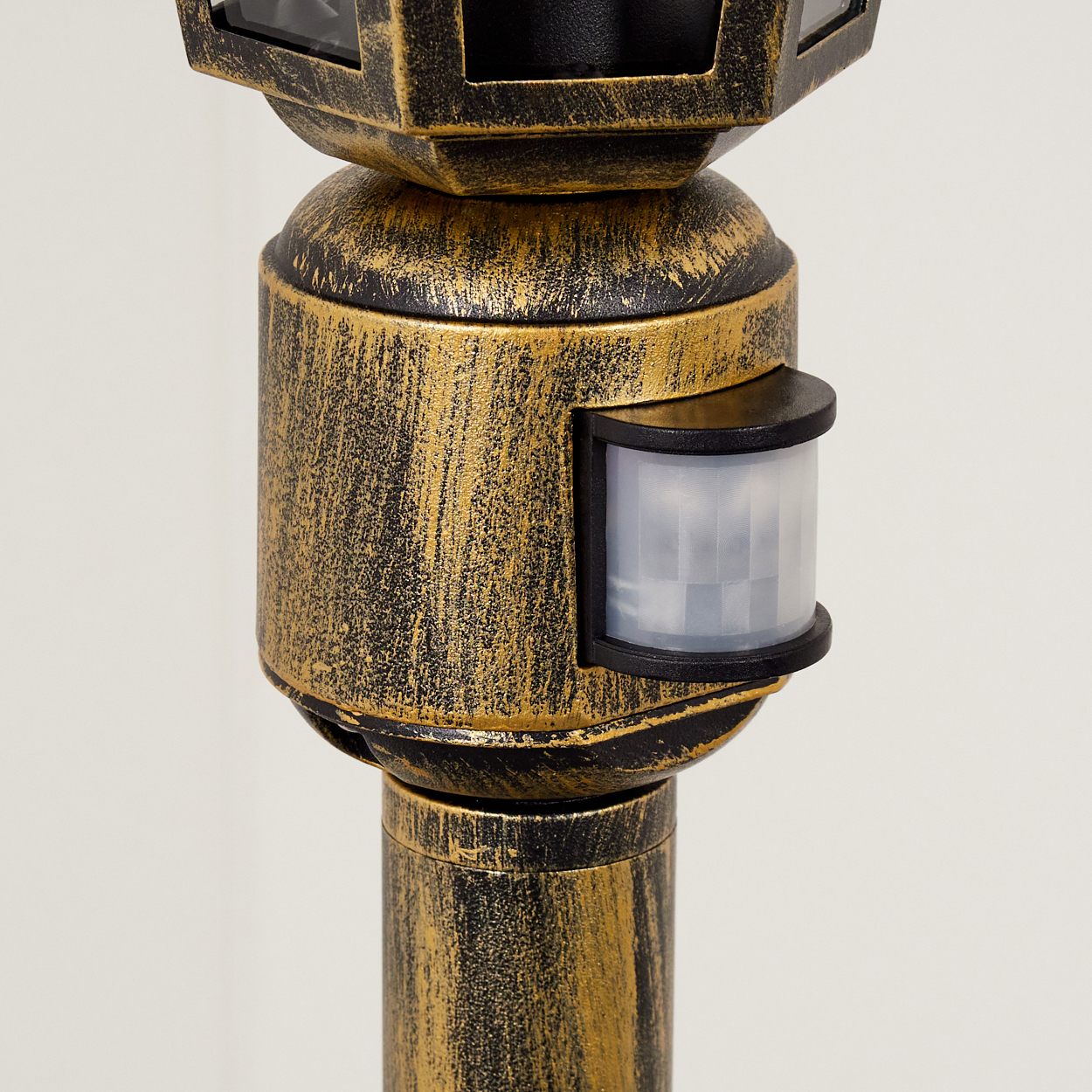 Nahaufnahme des Bewegungssensors und des Gehäuses einer Außenlampe, mit goldfarbener und schwarzer Textur.