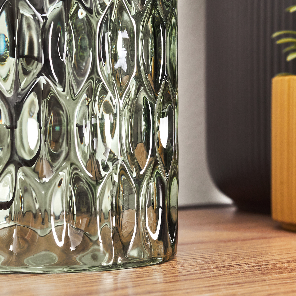 Nahaufnahme einer Vase aus klarem Glas mit einem ovalen Muster, auf einer Holzoberfläche stehend.