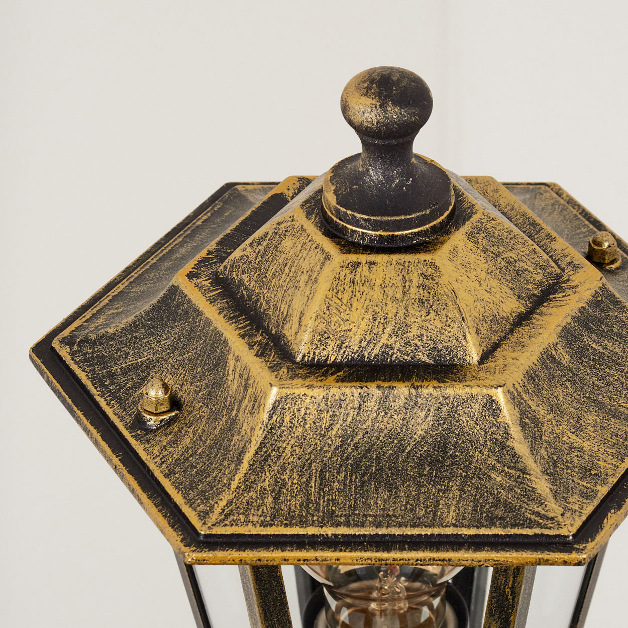 Nahaufnahme der Oberseite der Lampe mit gold-schwarzem Finish und sichtbarer Glühbirne.