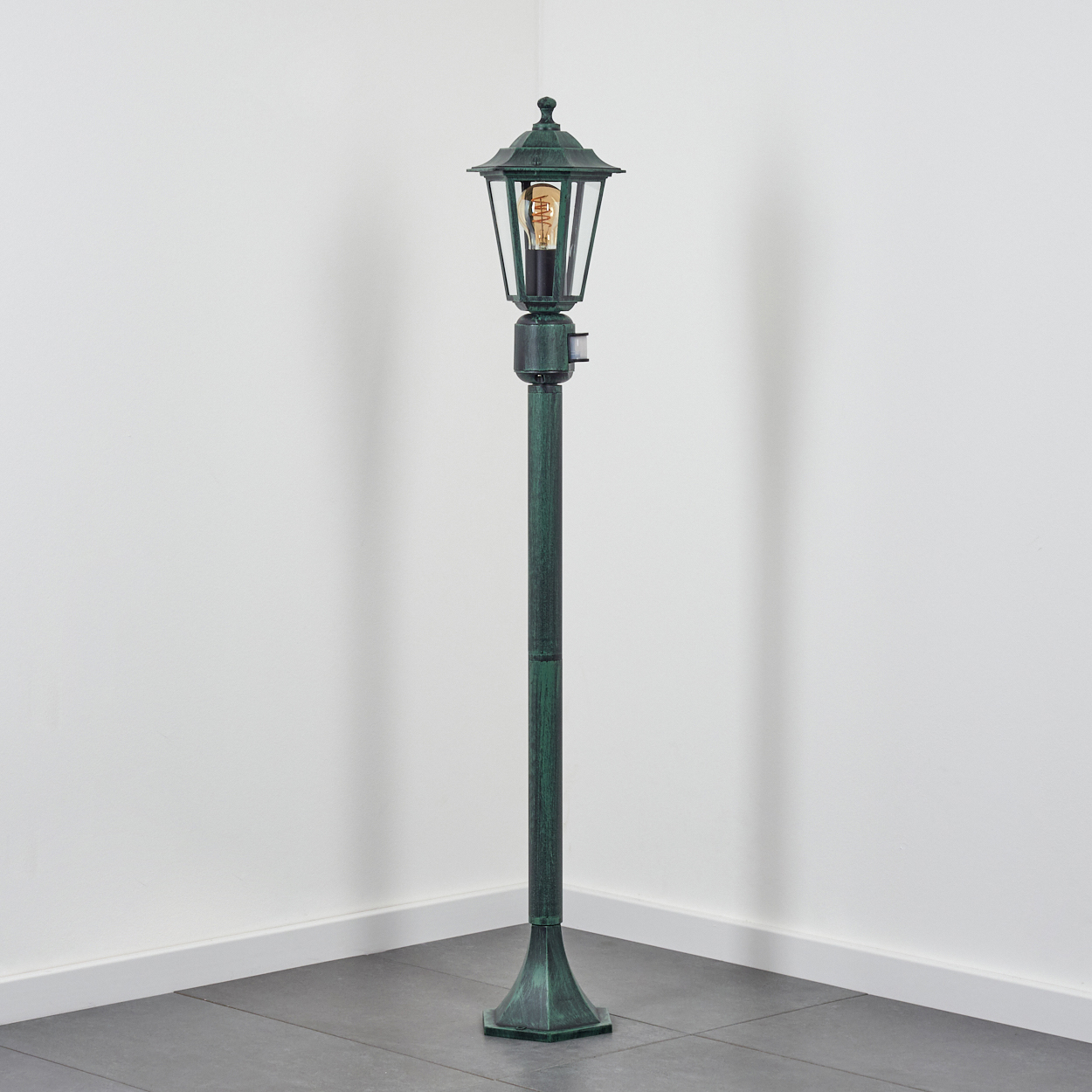 Eine Außenlampe, grün, in einer Ecke mit weißer Wand platziert.
