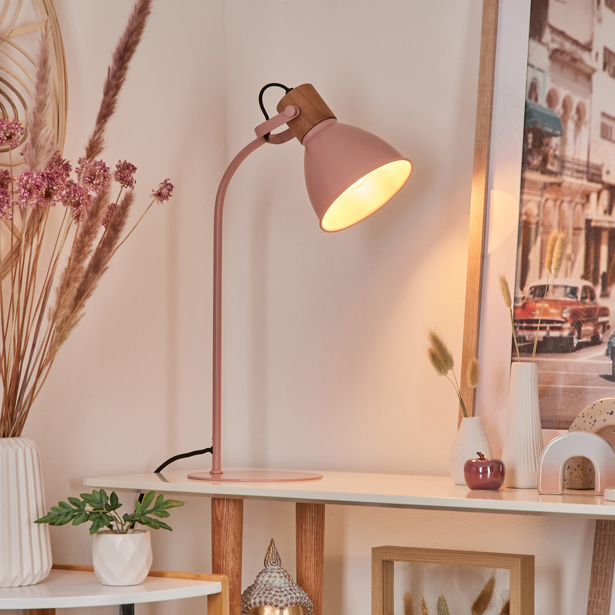 Eine rosa Schreibtischlampe mit Holzaufsatz, die eine weiße Oberfläche mit Dekorationen beleuchtet.