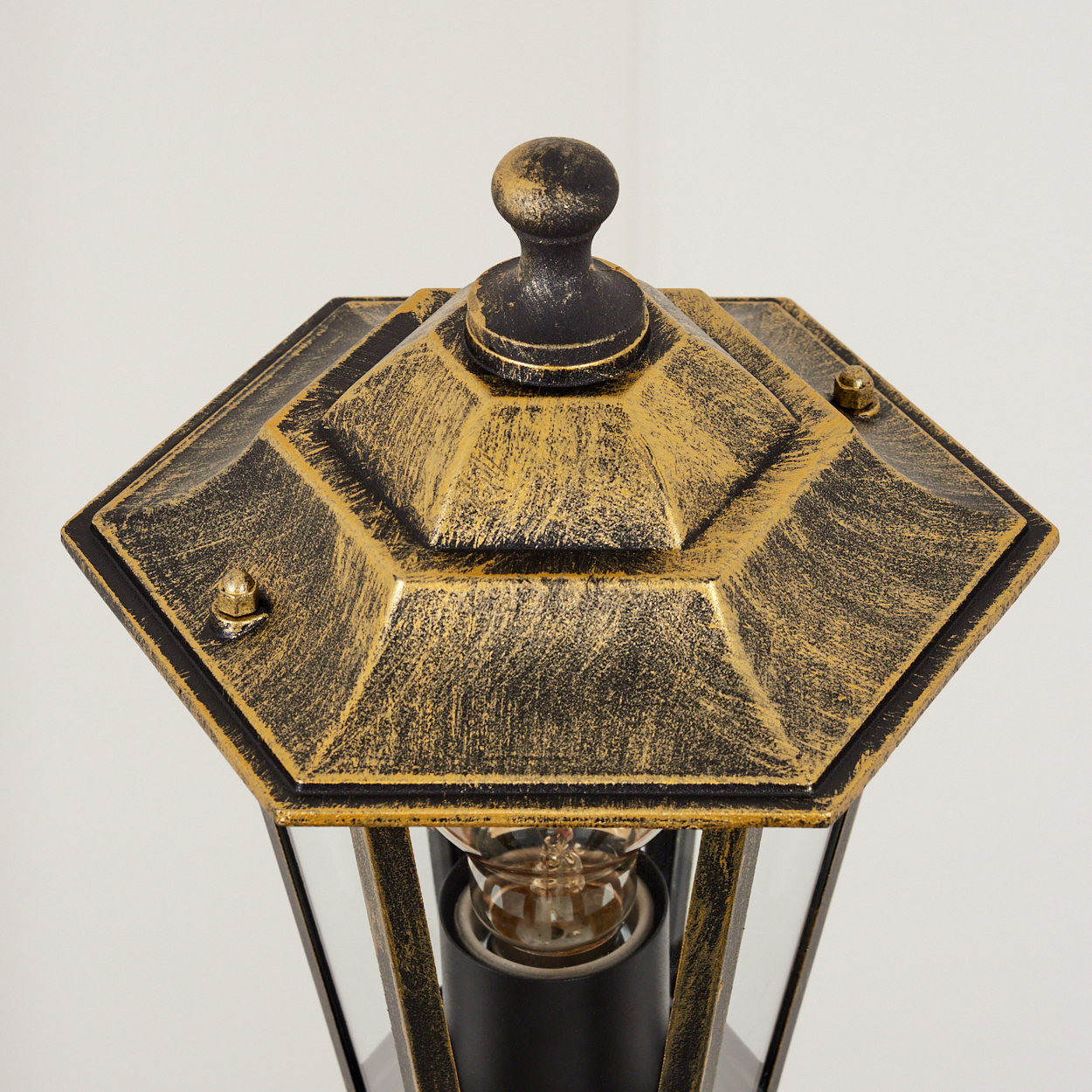 Nahaufnahme einer schwarzen und goldenen Außenlampe. Eine Glühbirne ist in der Lampe. Weißer Hintergrund.