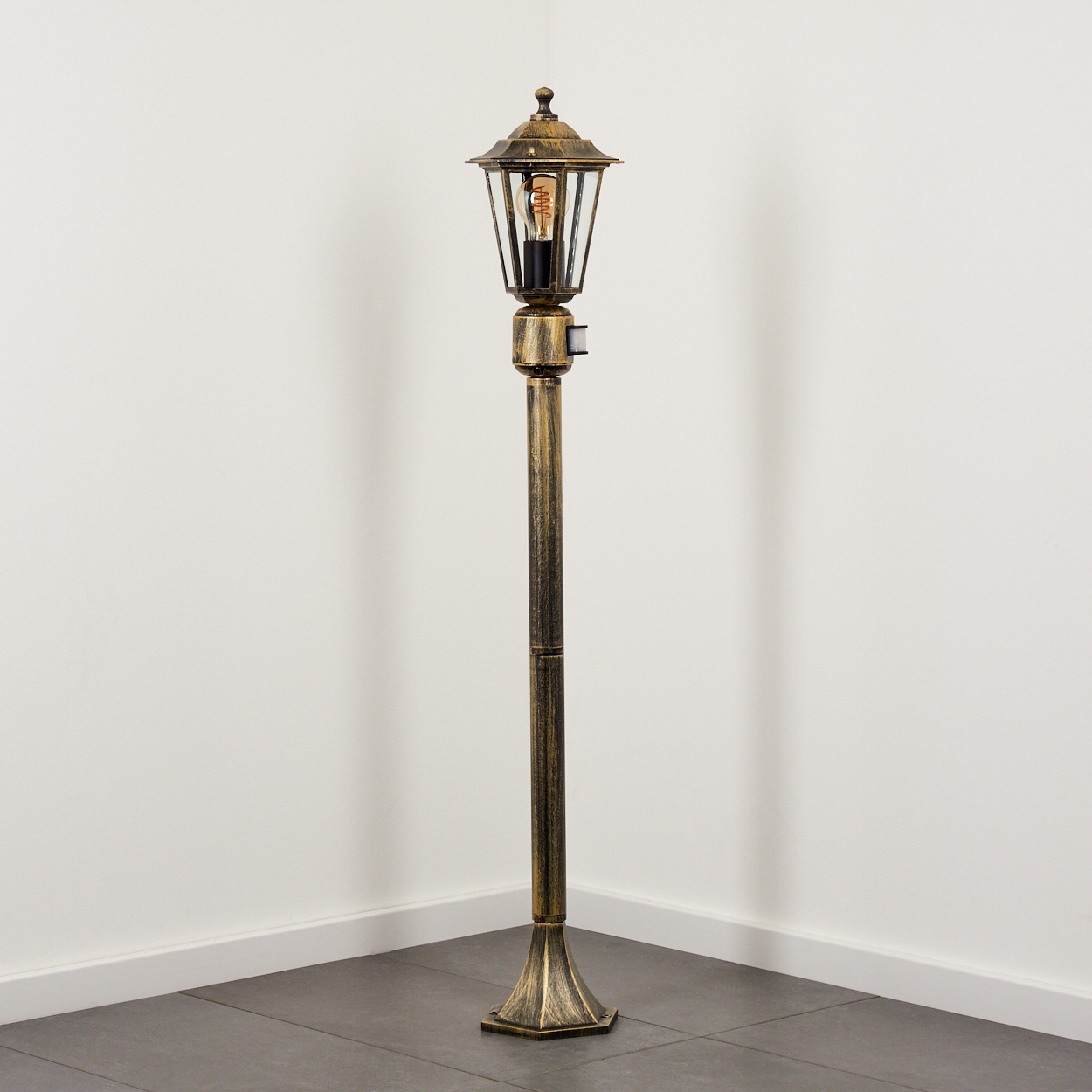 Außenlampe in der Ecke, Licht an. Gold- und Schwarzfarben. Weiße Wand und Boden.