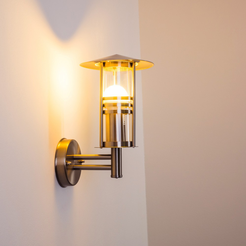 Eine an der Wand montierte Außenlampe mit zylindrischem Glasgehäuse und Metalloberfläche. Das Licht ist an.