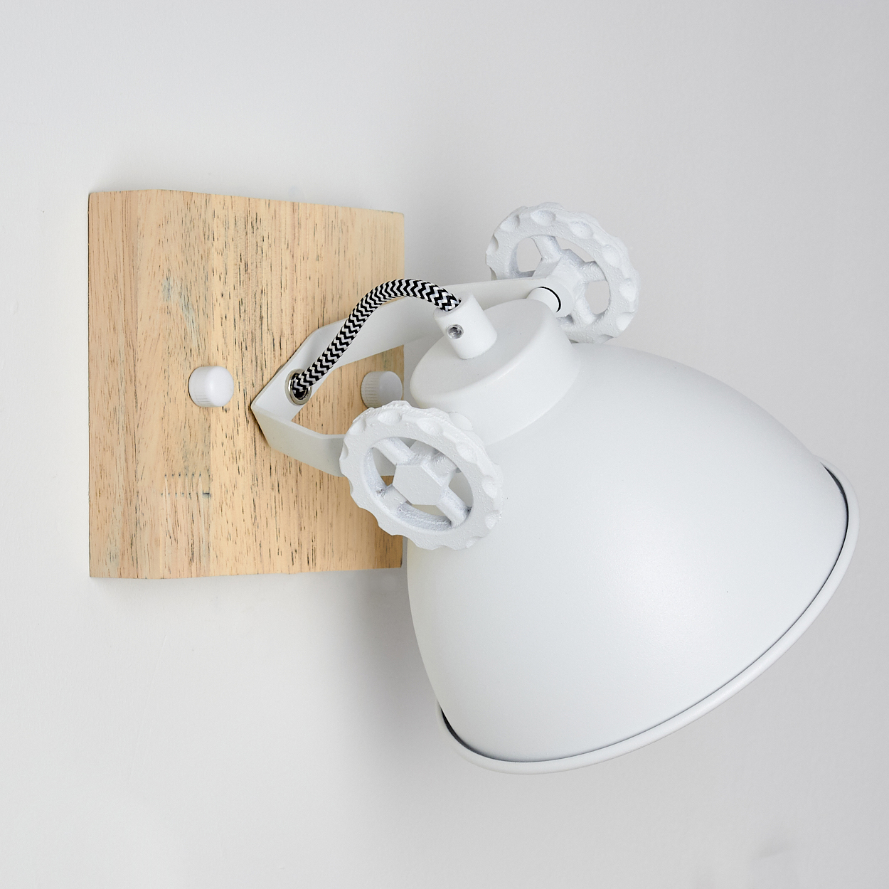 Eine weiße Wandleuchte mit Holzsockel. Die Lampe ist abgewinkelt.