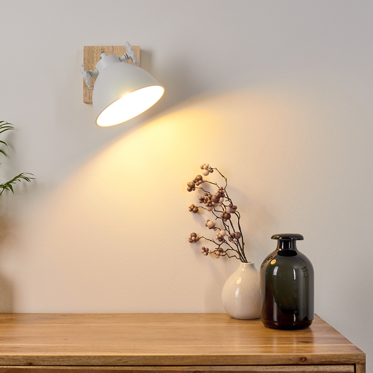Weiße Wand. Weiße Wandlampe mit Licht. Eine Vase und eine Pflanze.