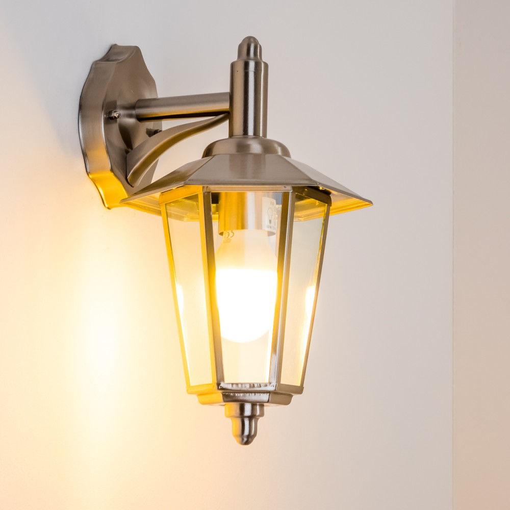 Beleuchtete silberne Außenwandleuchte, die ein warmes Licht auf eine weiße Wand wirft.