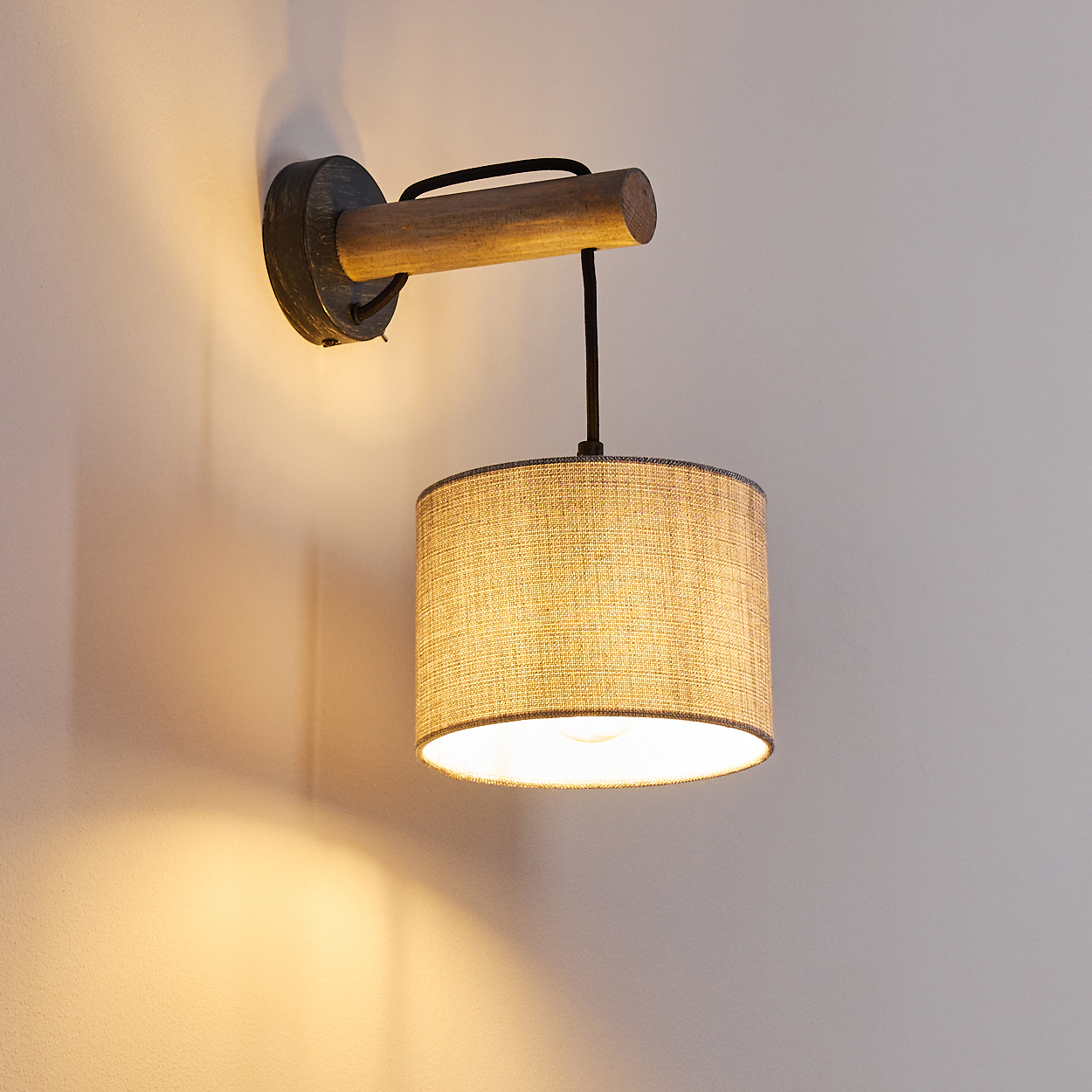 Eine Holzlampe mit zylindrischem Lampenschirm beleuchtet eine hellfarbige Wand.