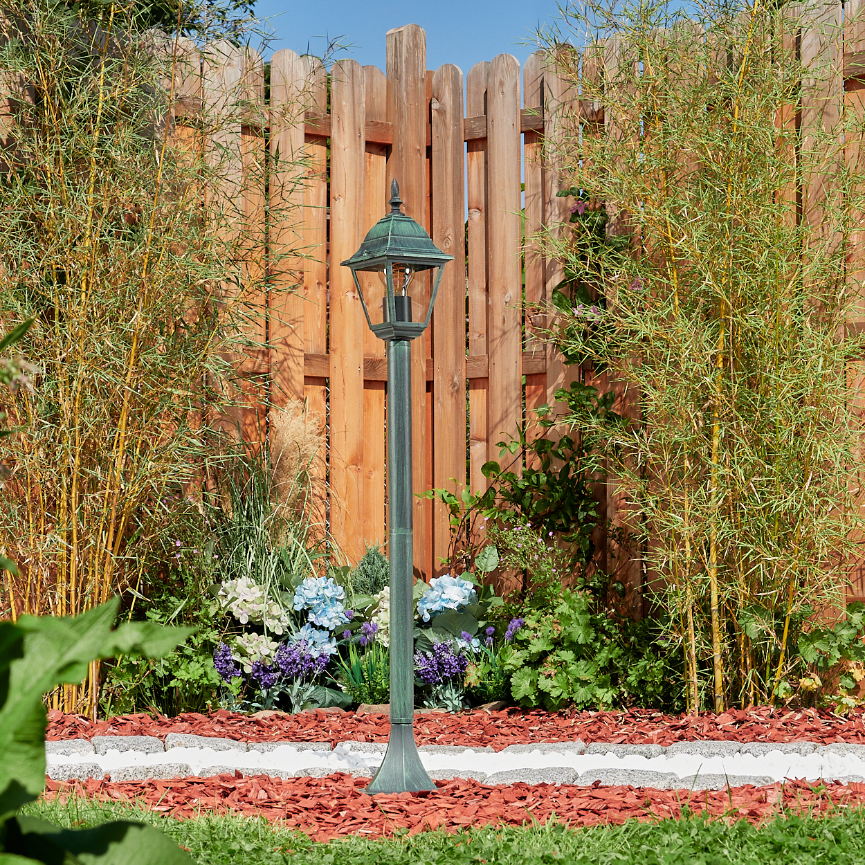Außenlaterne in einem Garten mit Holzzaun und Bambuspflanzen.