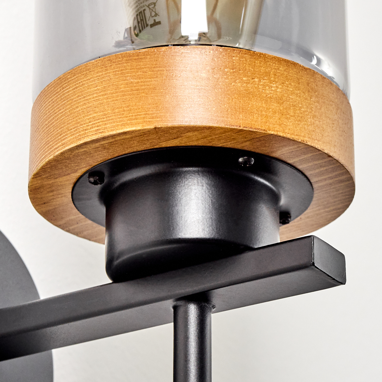 Nahaufnahme einer schwarzen Wandlampe mit Holzakzent und einem klaren Glaszylinder.