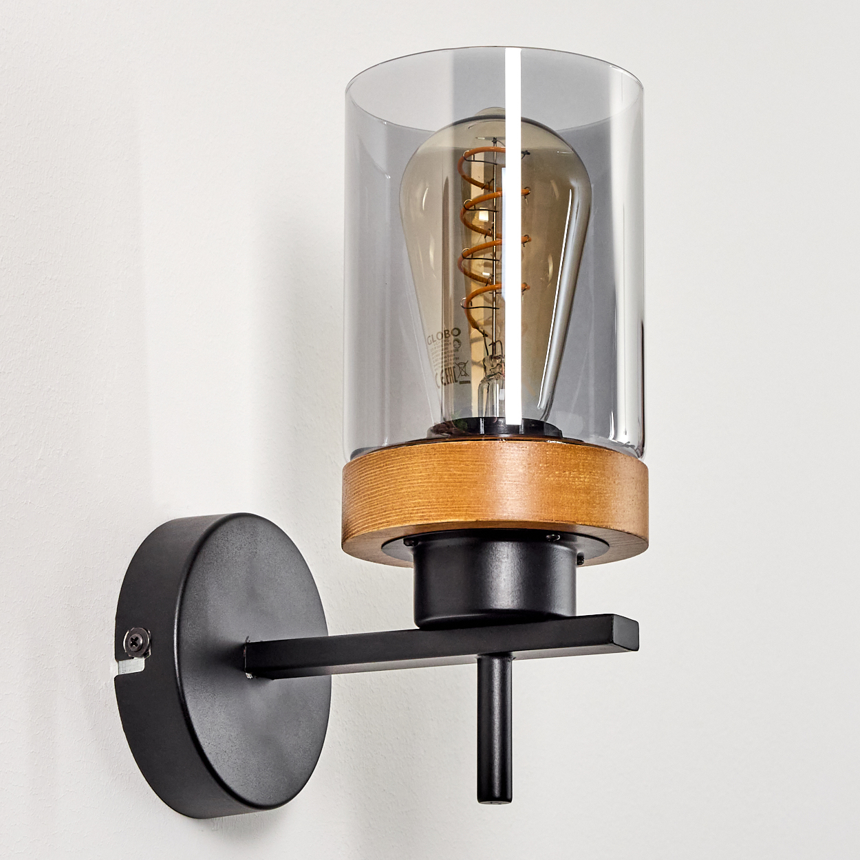 Eine schwarze Wandlampe mit Holzakzent und einem klaren Glaszylinder. Eine Edison-Glühbirne ist innen.