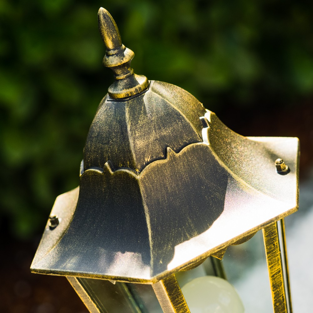 Nahaufnahme eines detaillierten, goldfarbenen Lampenaufsatzes mit kompliziertem Design, vor Grün.