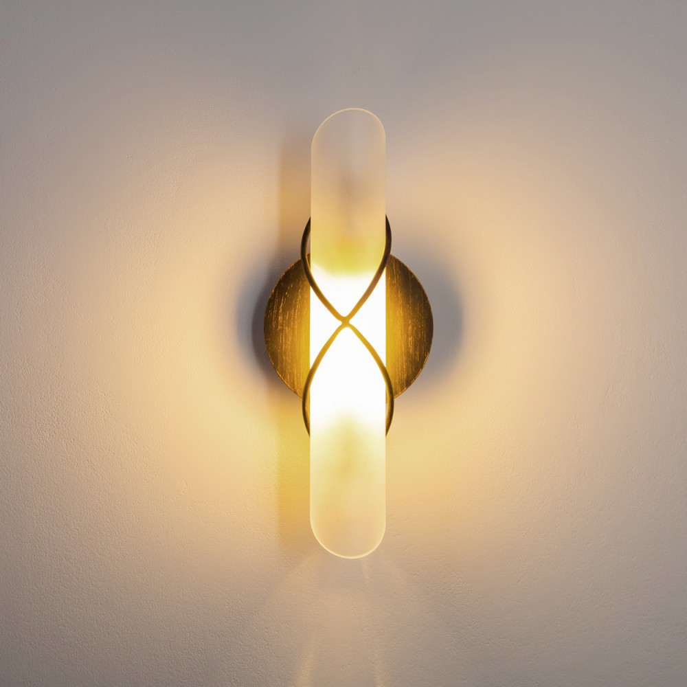 Wandleuchte mit einem Milchglasrohr und einem goldenen Rahmen, beleuchtet vor neutralem Hintergrund.