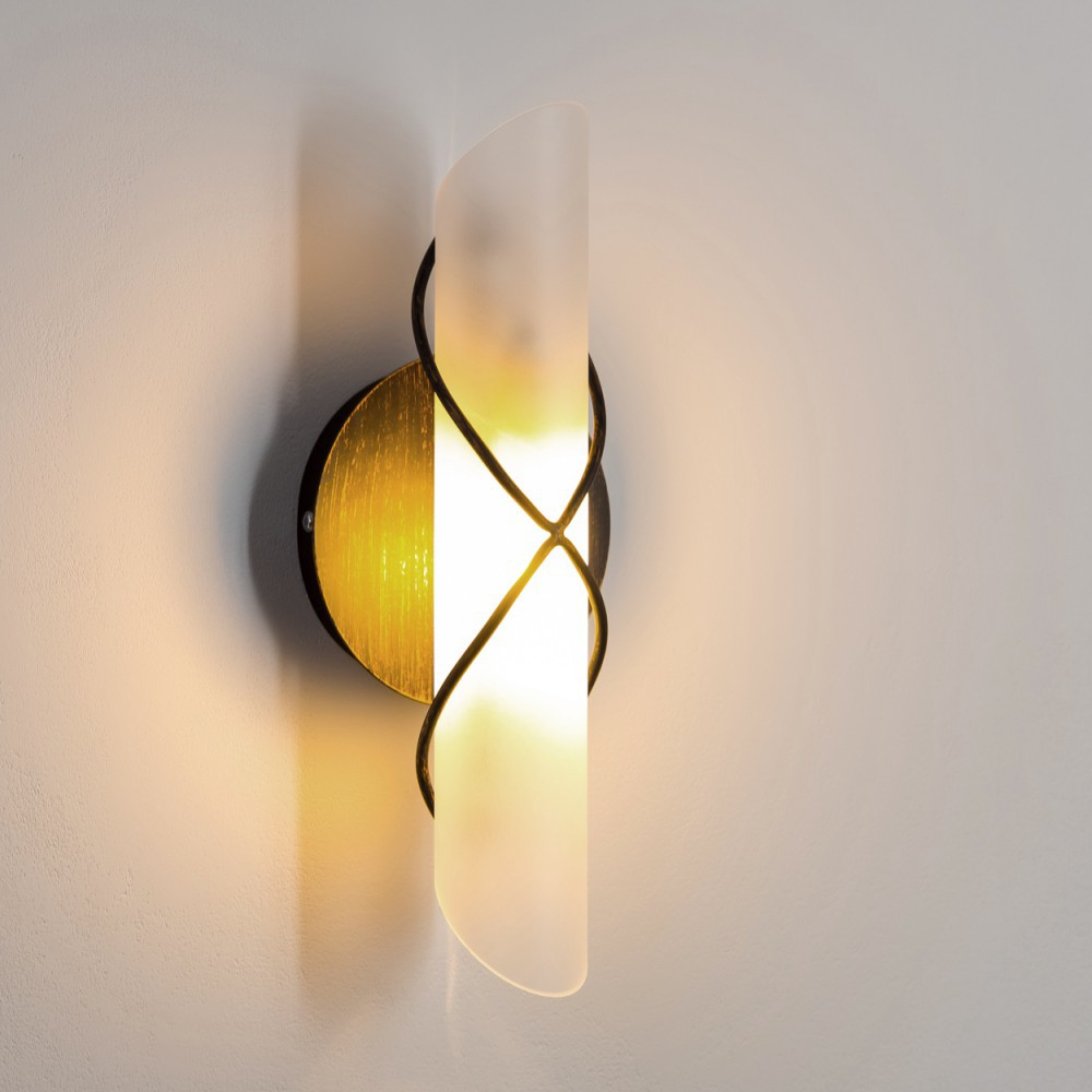 Eine Wandlampe mit Milchglasschirm und goldenen Akzenten, an einer weißen Wand.