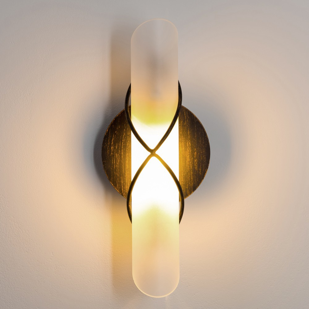 Eine Wandlampe mit bronzefarbenem Rahmen und einem Schirm aus Milchglas, an einer weißen Wand montiert.