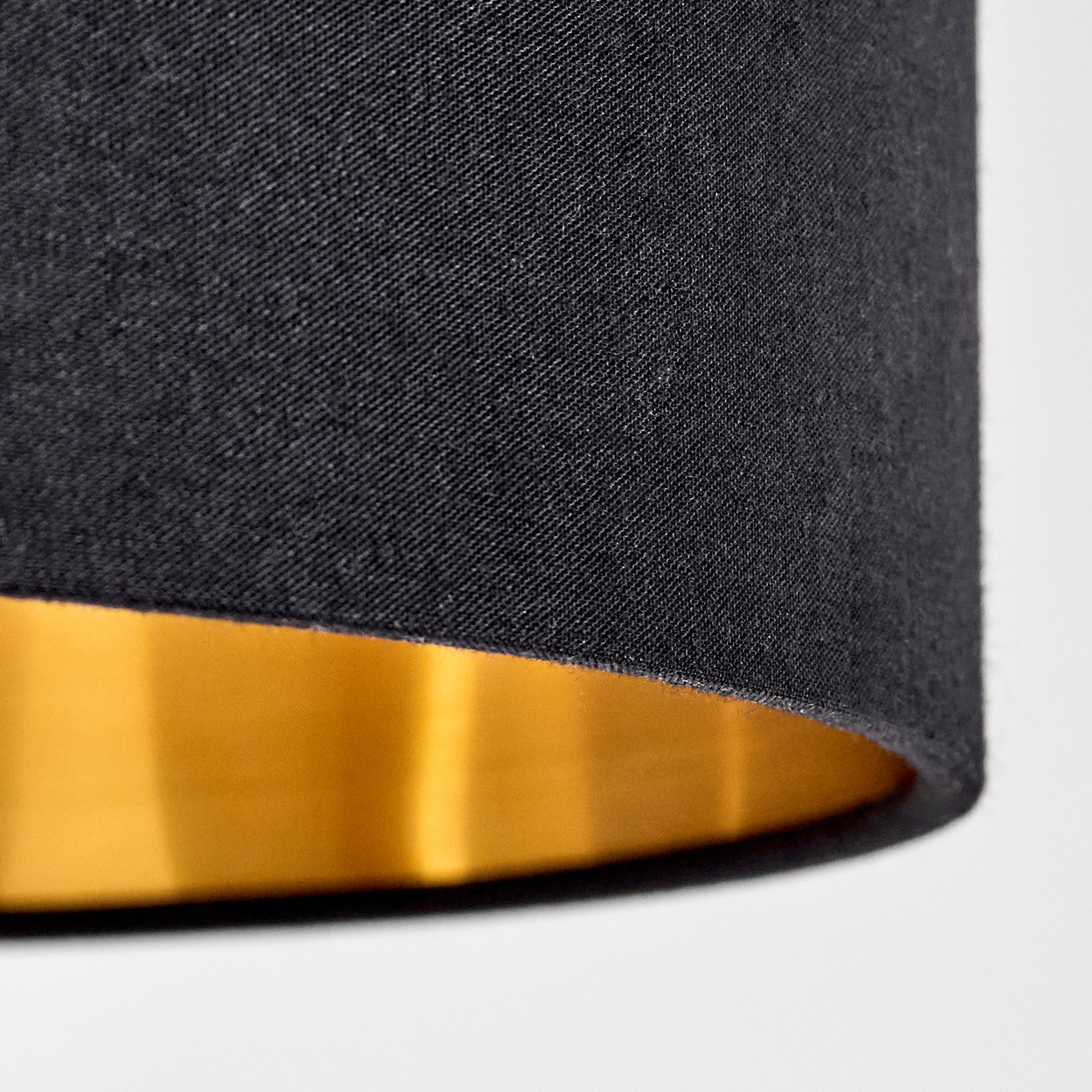 Nahaufnahme eines schwarzen Lampenschirms mit goldenem Innenraum. Hintergrund: weiße Oberfläche.