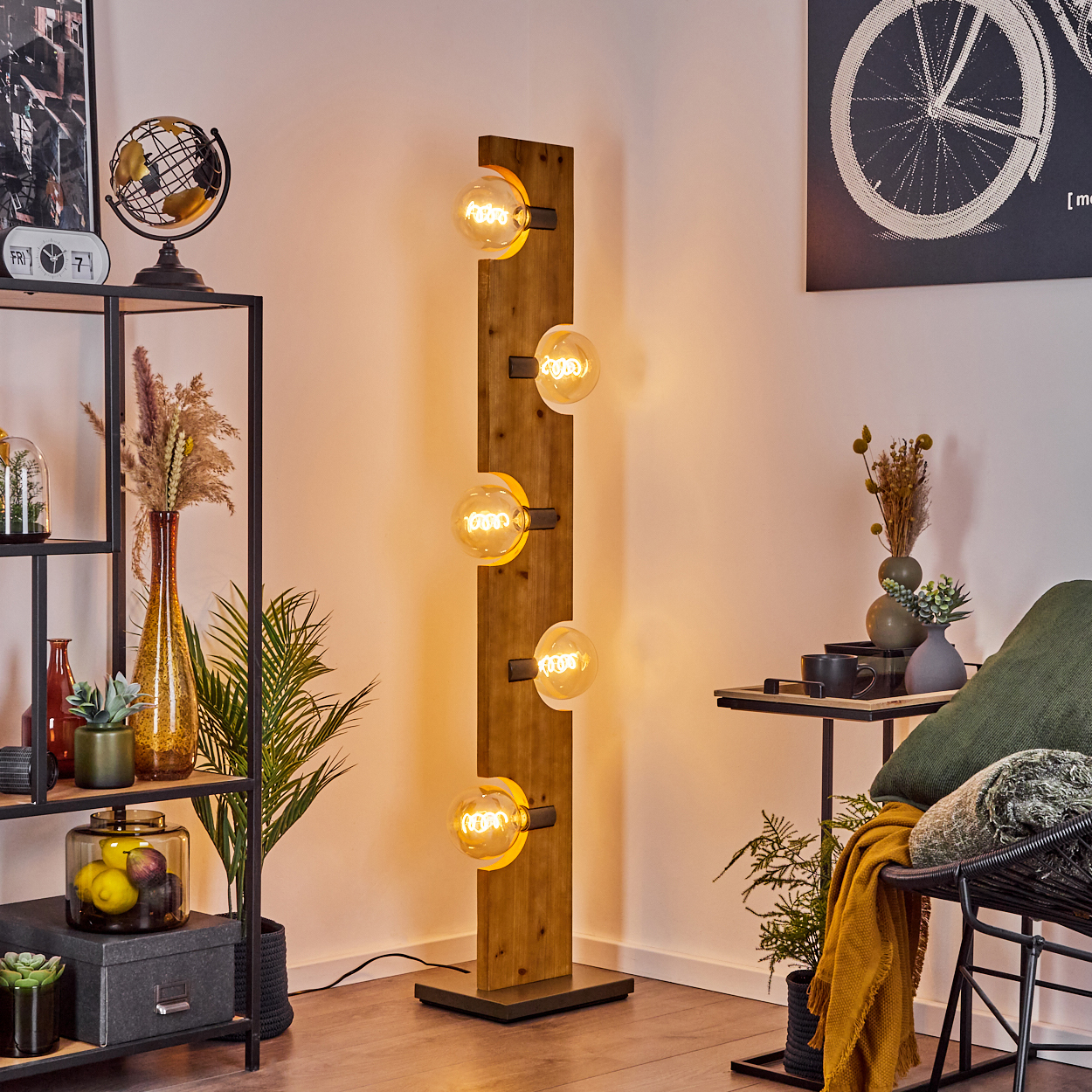 Eine Stehlampe mit vier Glühbirnen auf einer Holzkonstruktion. Es gibt einen Globus, Pflanzen und ein Regal.