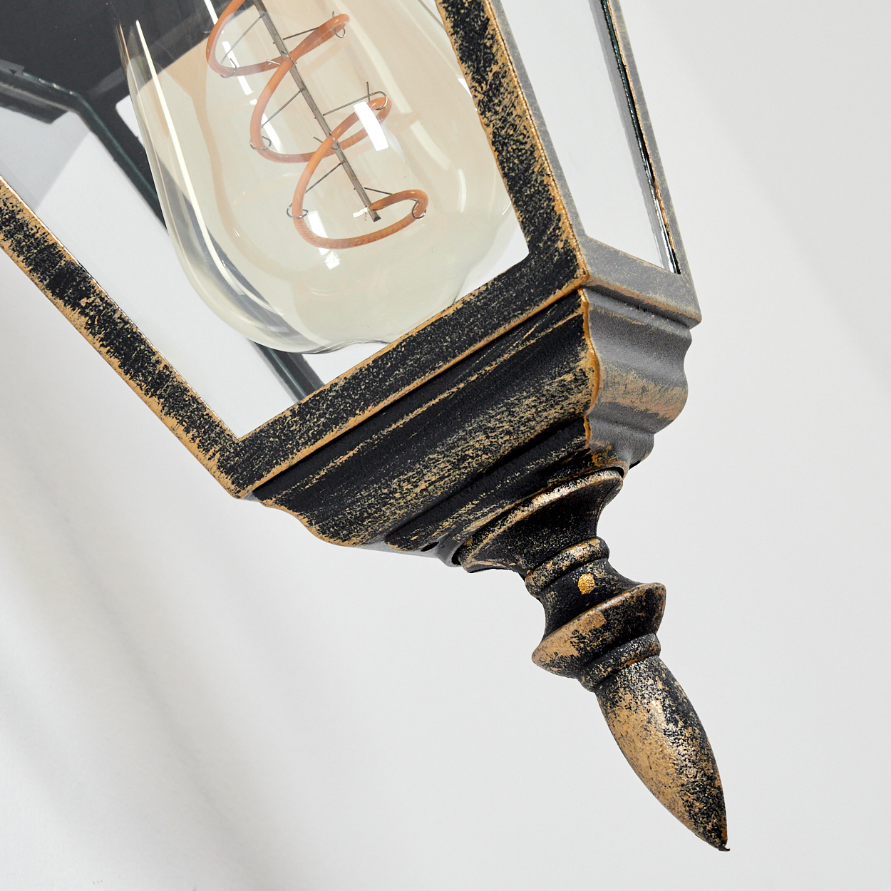 Nahaufnahme einer goldfarbenen Außenlampe mit klarem Glasgehäuse, das eine Glühbirne zeigt.