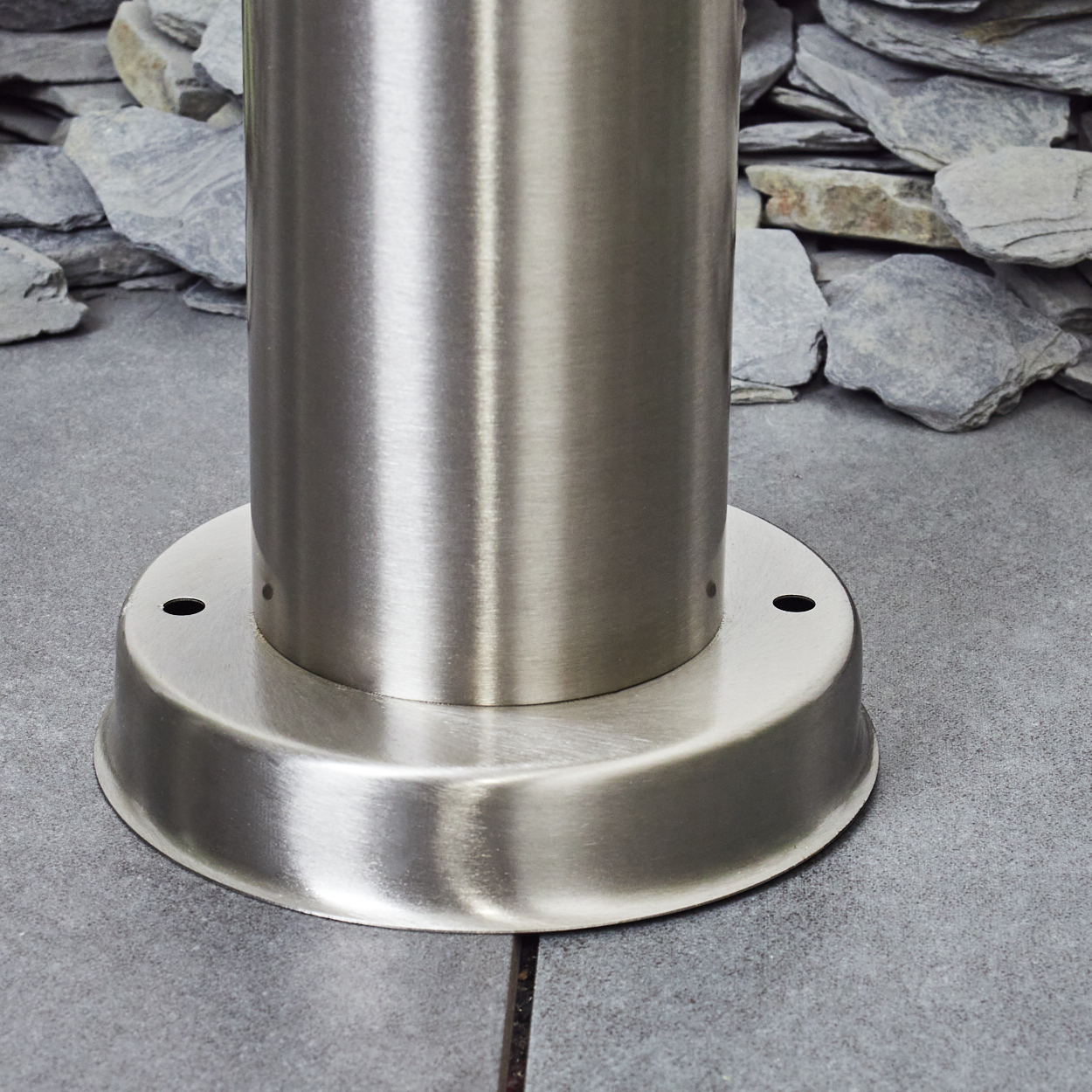 Nahaufnahme eines Metallsockels und einer zylindrischen Lampenstange auf grauer Steinoberfläche. Der Hintergrund ist unscharf.