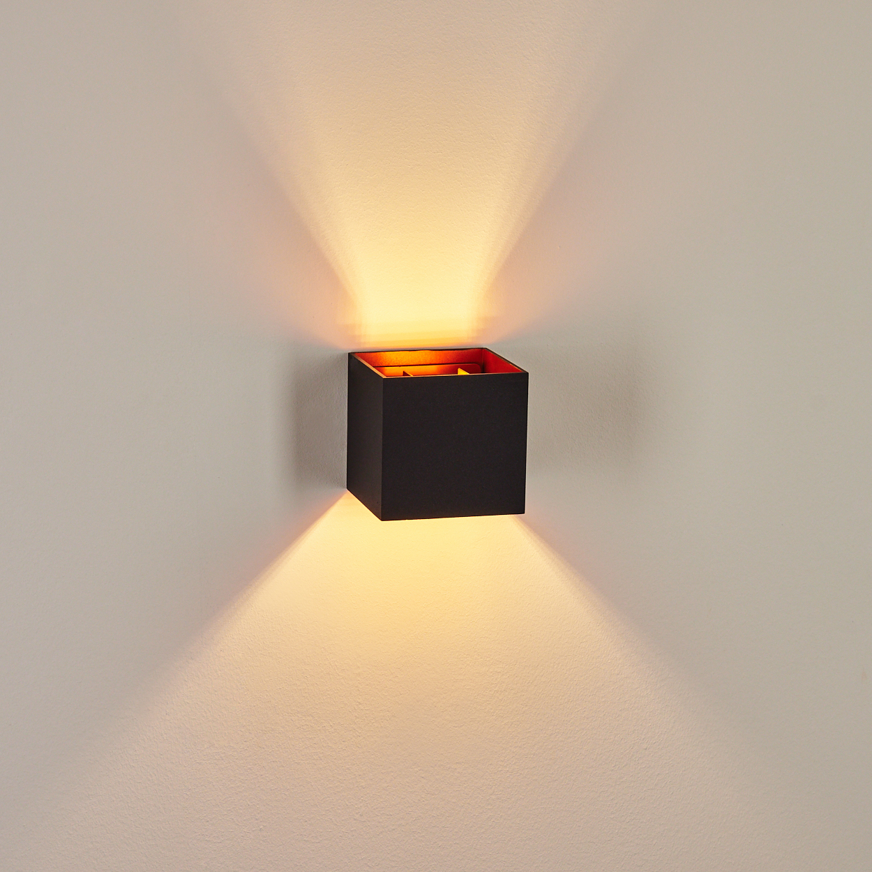 Eine schwarze, würfelförmige Wandleuchte mit hellem orangefarbenen Innenraum, wirft Licht nach oben und unten.