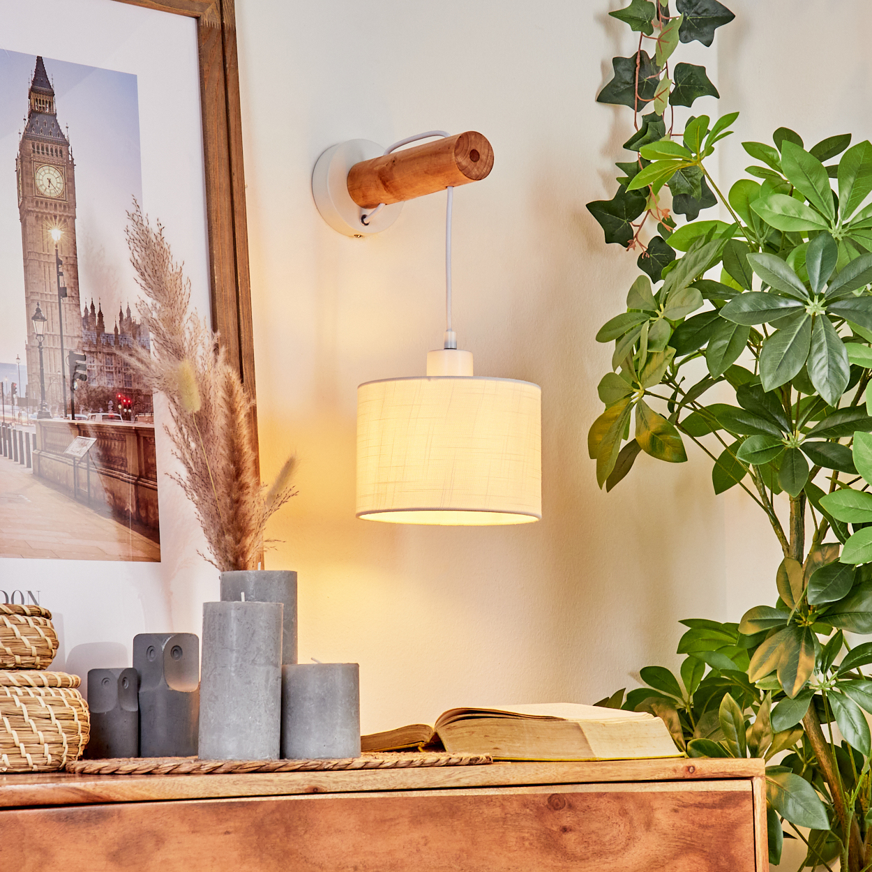 Wandlampe mit Holzarm, beigem Lampenschirm und Big Ben Bild im Hintergrund. Kerzen und Buch auf Regal.