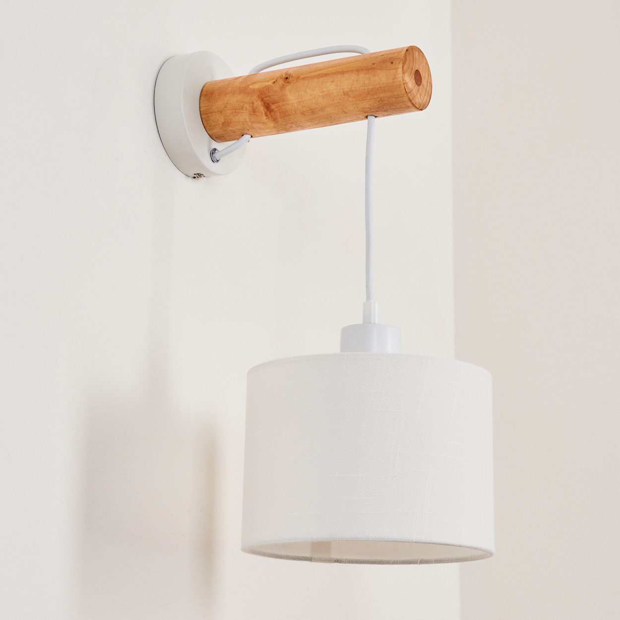 Eine weiße Wandleuchte mit einem Arm aus Holz zylinder und einem weißen Lampenschirm, der unten hängt.