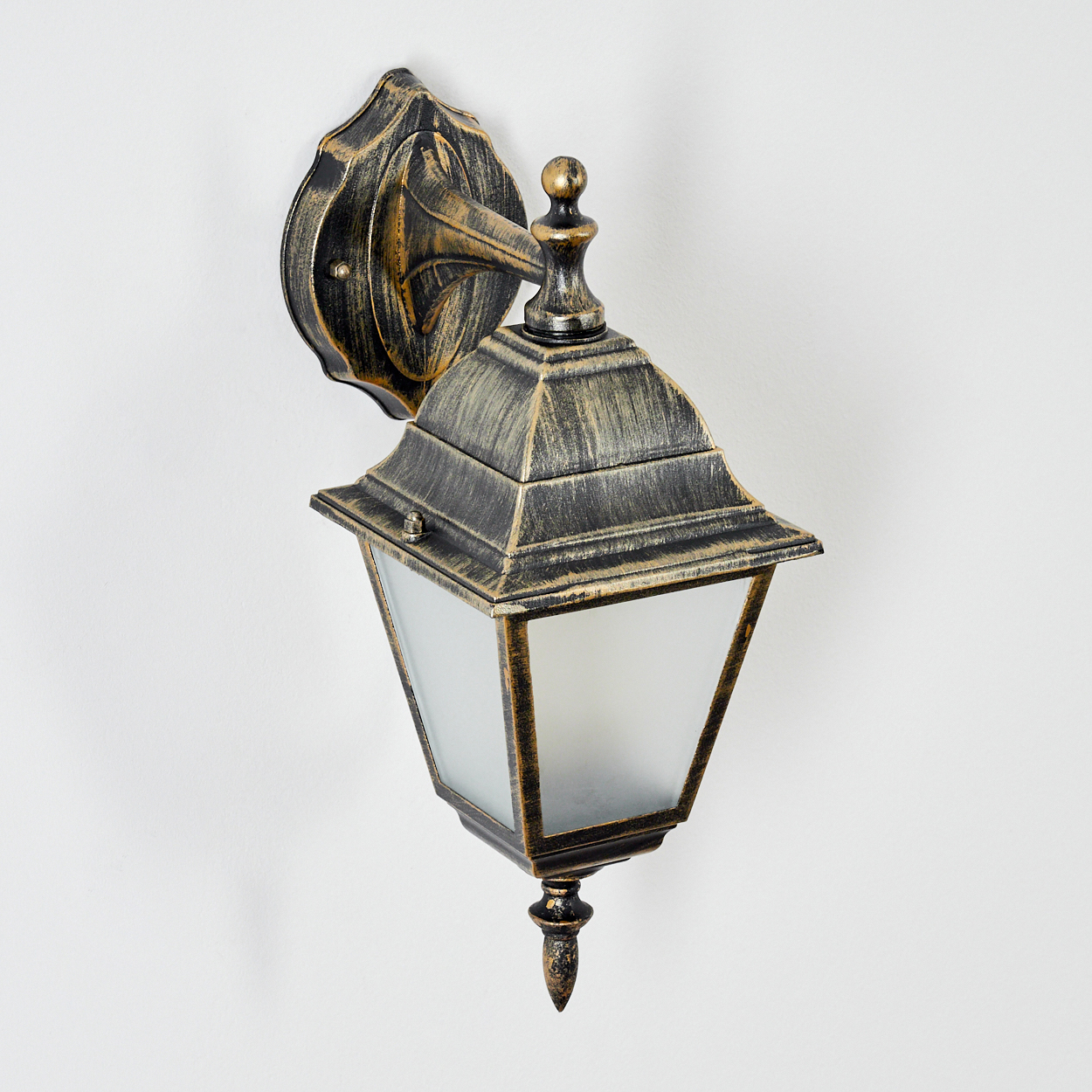 Nahaufnahme einer schwarz-goldenen Wandleuchte. Die Lampe hat eine Glasfront und ist an einer weißen Wand montiert.