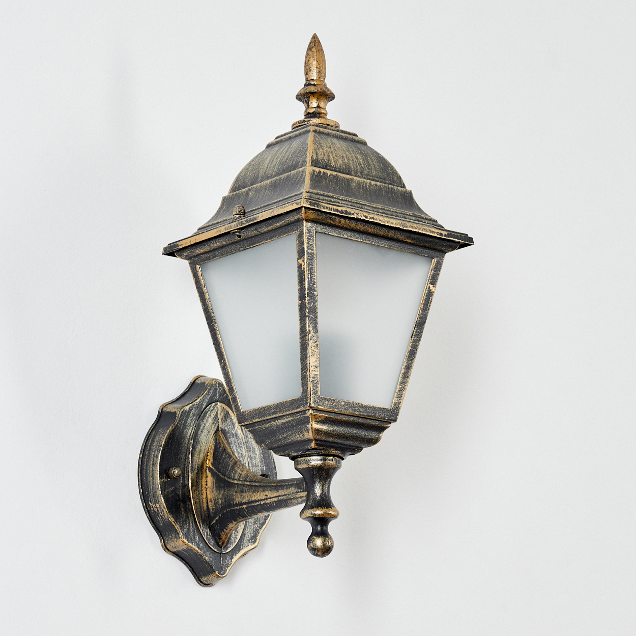 Eine schwarz-goldene Wandleuchte. Die Lampe hat eine Glasfront und ist an einer weißen Wand montiert.