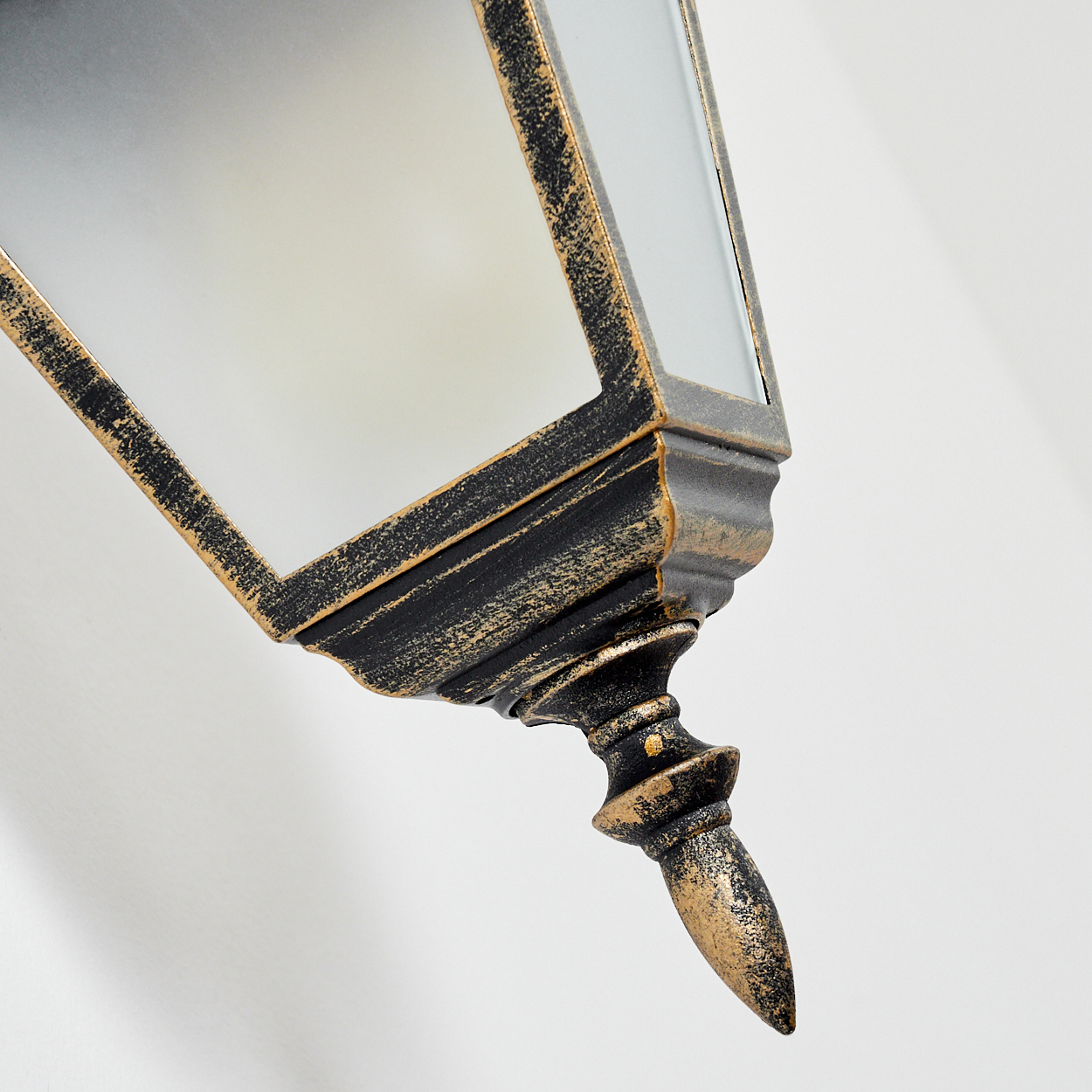 Nahaufnahme einer schwarz-goldenen Wandleuchte. Die Lampe hat eine Glasfront und ist an einer weißen Wand montiert.