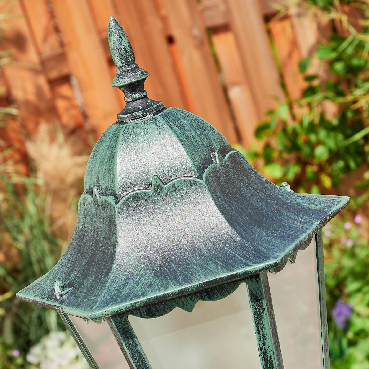 Nahaufnahme der Oberseite eines grünen und schwarzen Außenlampenpfostens. Die Lampe hat eine Glasfront.