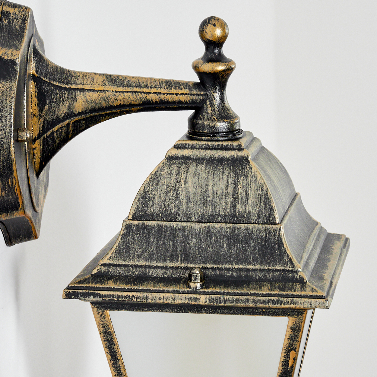 Nahaufnahme des oberen Teils einer goldenen Wandlampe vor einer weißen Wand.