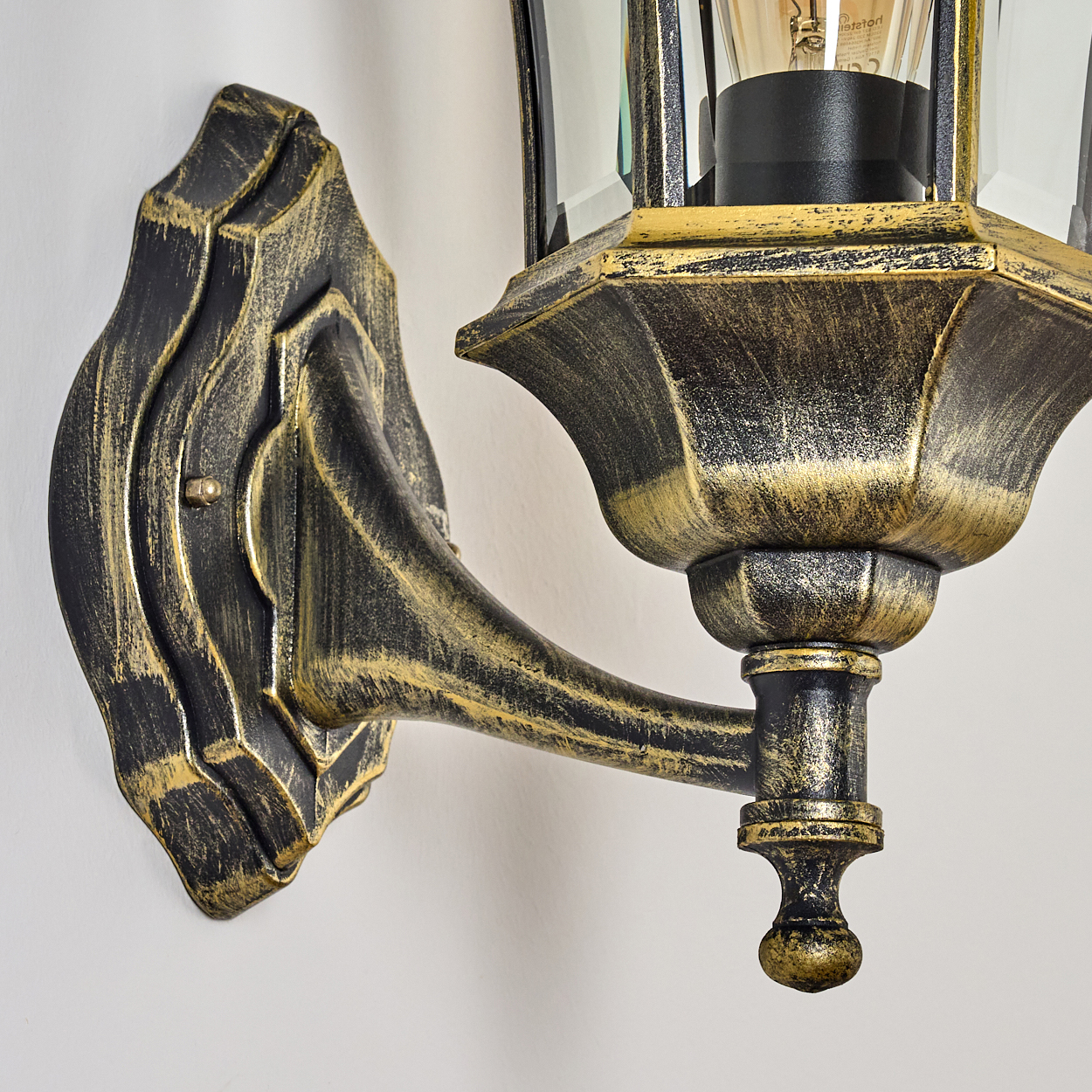 Nahaufnahme einer schwarz-goldenen Wandleuchte. Die Lampe hat eine Glasfront und eine leuchtende Glühbirne.