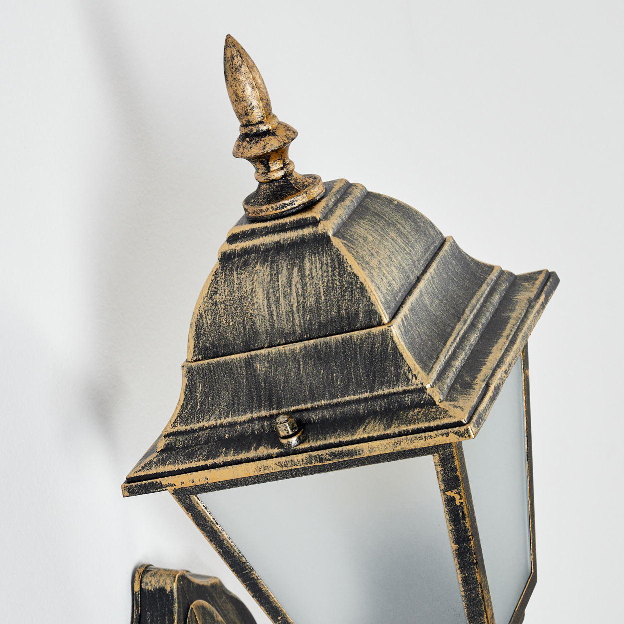 Nahaufnahme einer goldenen Wandlampe, die den oberen Teil vor einer weißen Wand zeigt.