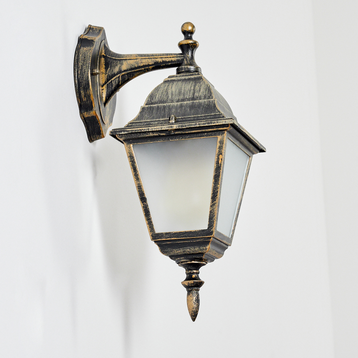 Goldfarbene Wandlampe an weißer Wand, mit Milchglasschirm. Die Lampe ist beleuchtet.
