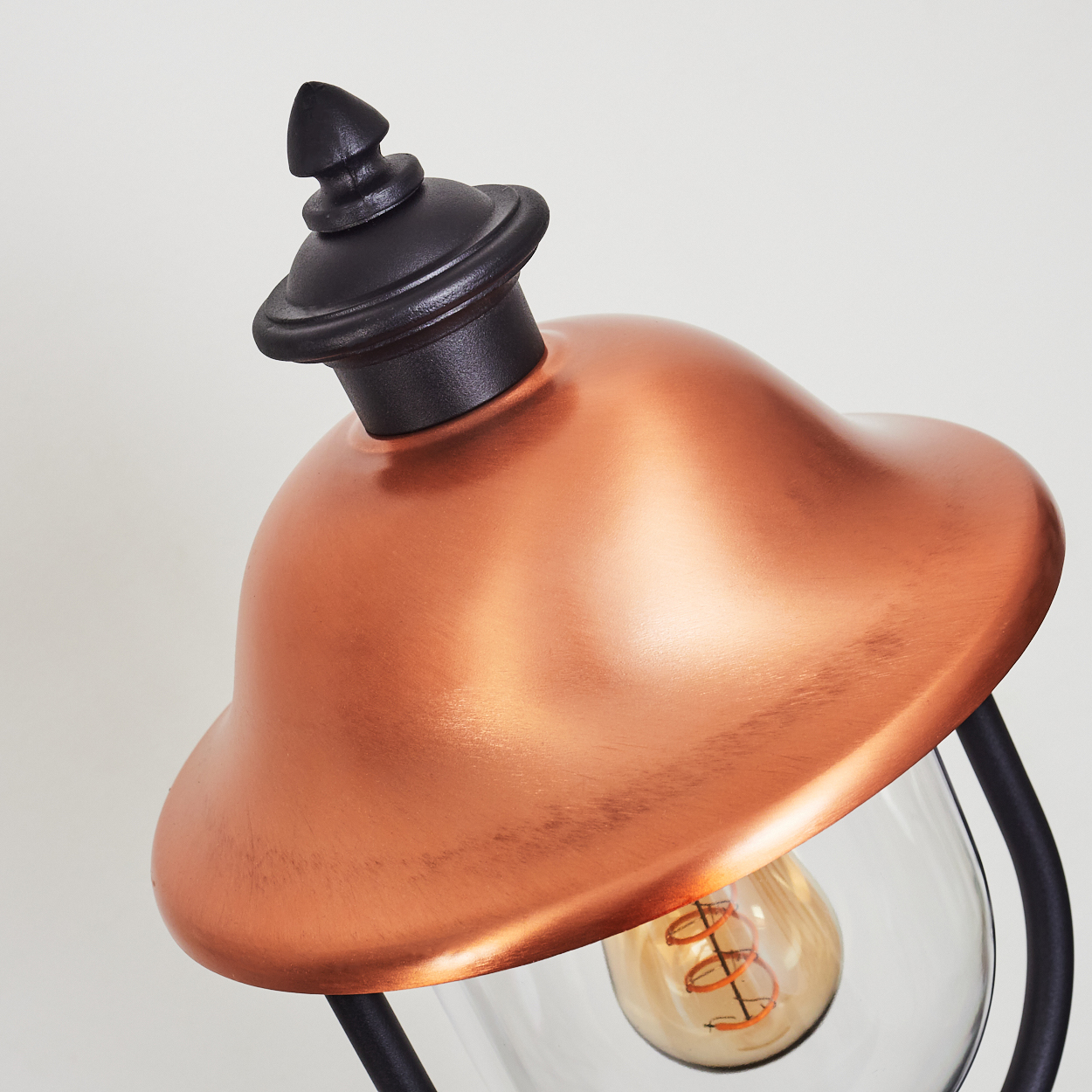 Nahaufnahme einer Lampe mit Kupferaufsatz und klarem Glasschirm. Glühbirne sichtbar.