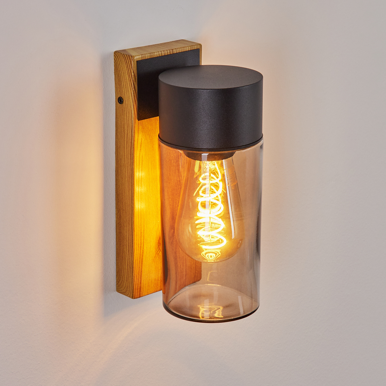 Wandleuchte mit Holzsockel und schwarzem Aufsatz. Die Lampe ist zylindrisch mit Glühbirne.