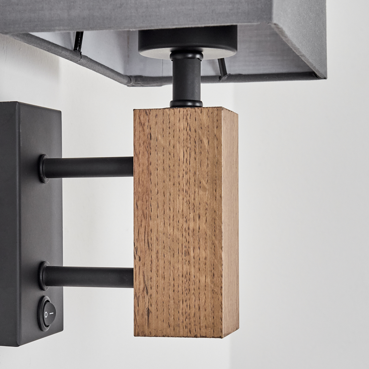 Eine Wandleuchte mit grauem, rechteckigem Schirm, Holzelementen und einem schwarzen Sockel mit Schalter.