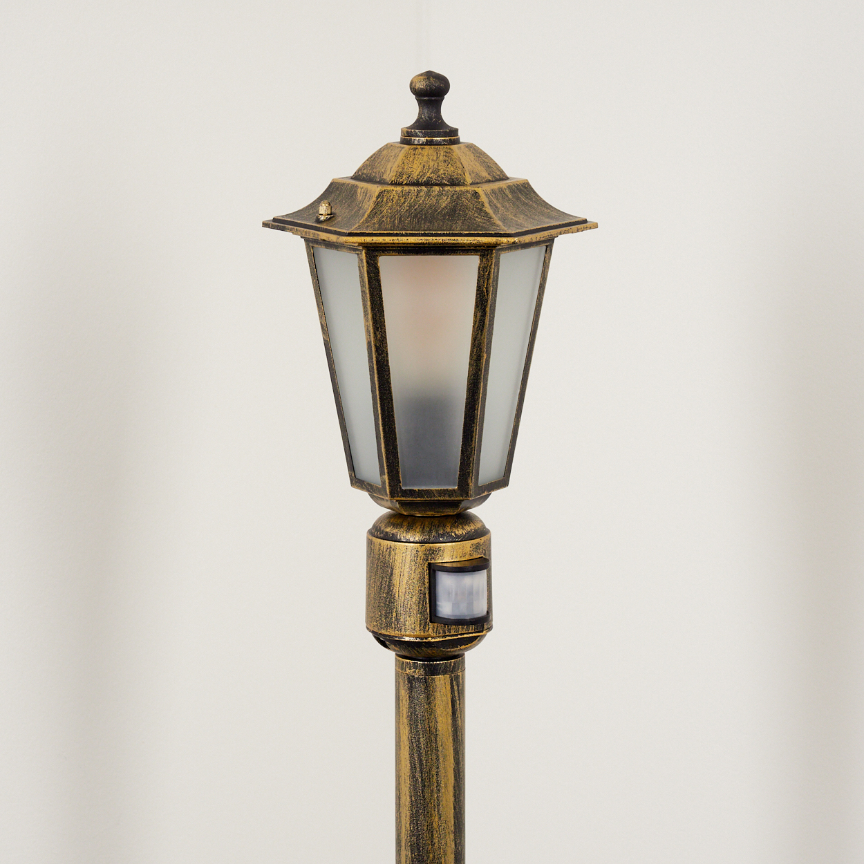 Eine Außenlaterne mit goldener Oberfläche. Sie hat ein Gehäuse aus Milchglas und einen Bewegungssensor.
