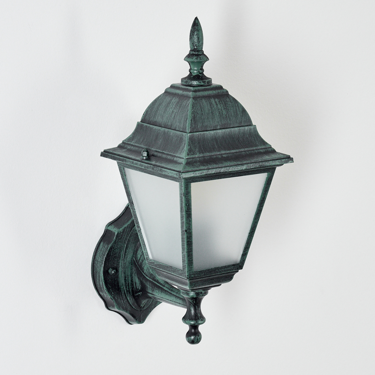 Grüne Wandlampe mit Milchglas. Die Lampe ist an einer weißen Wand montiert. Der Lampenpfosten ist gebogen.