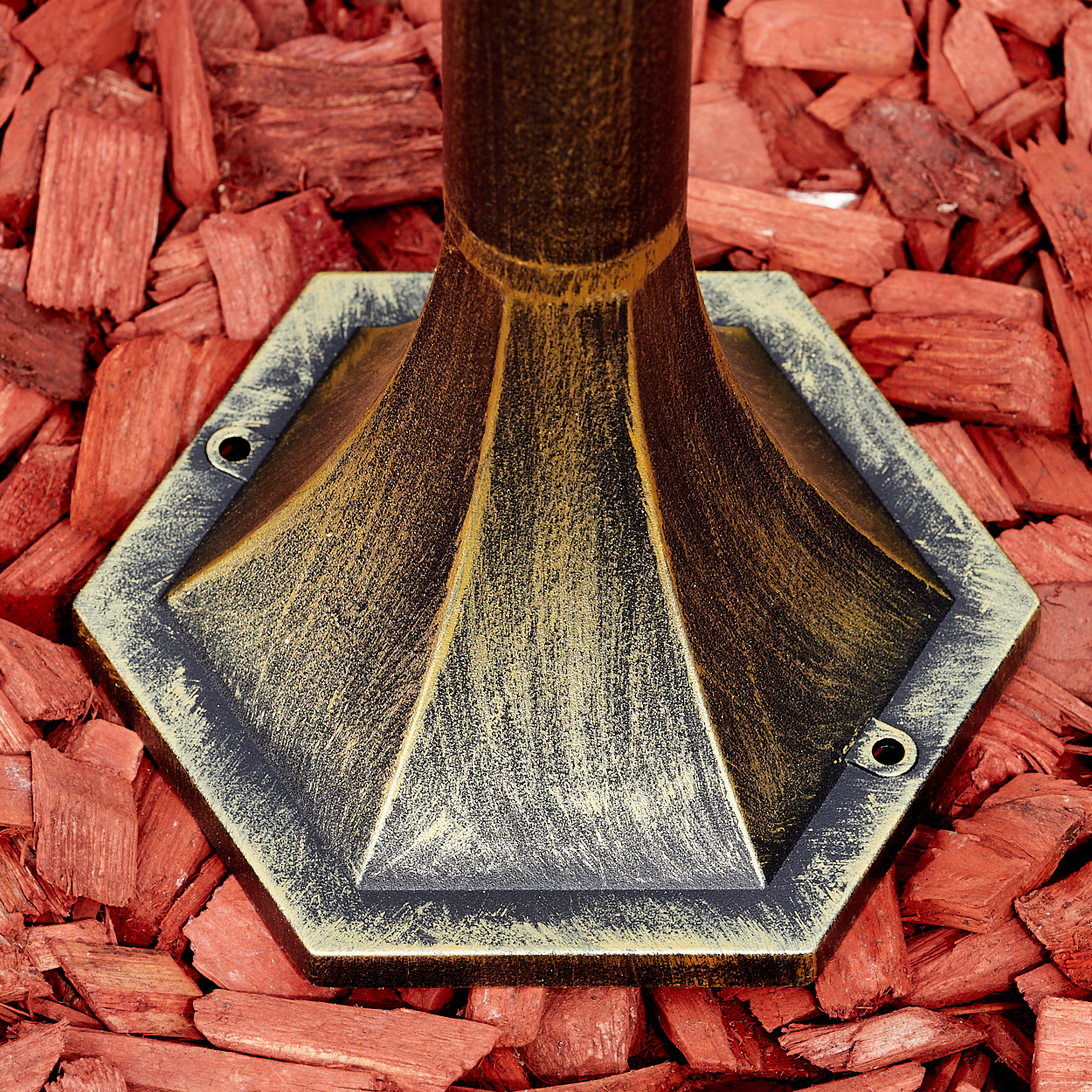 Ein Lampensockel auf roten Holzspänen, mit Gold- und Schwarzlack, sechseckige Form.