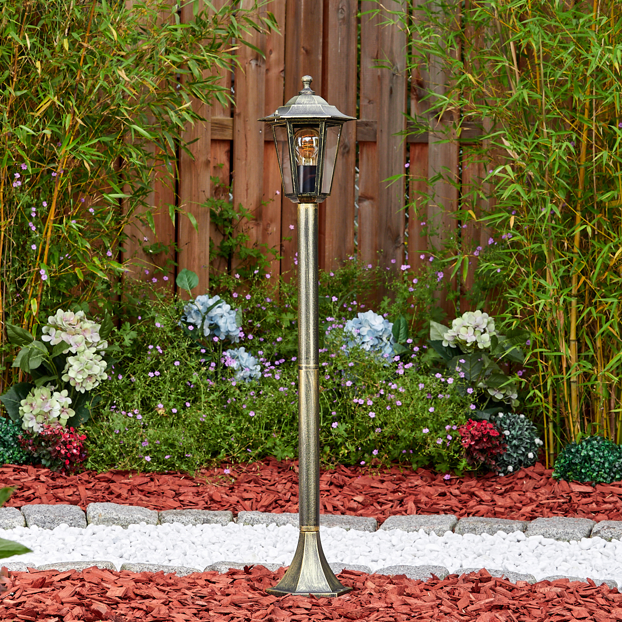 Eine hohe Außenlaterne in einem Garten. Die Lampe hat eine dekorative Spitze und Glasscheiben.