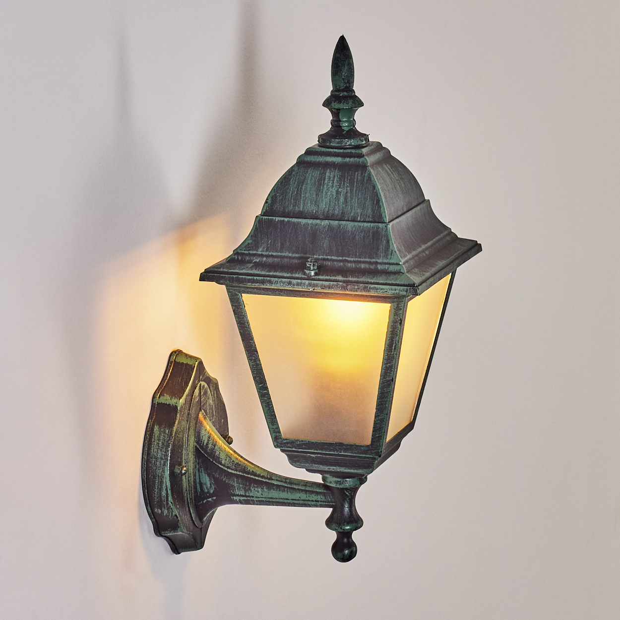 Außenwandleuchte. Grüne Farbe mit Milchglas. Die Lampe ist an einer weißen Wand montiert und beleuchtet.