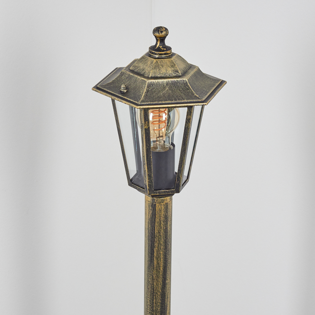 Eine Außenlaterne mit Gold-Finish. Die Lampe hat eine dekorative Spitze und klares Glas.