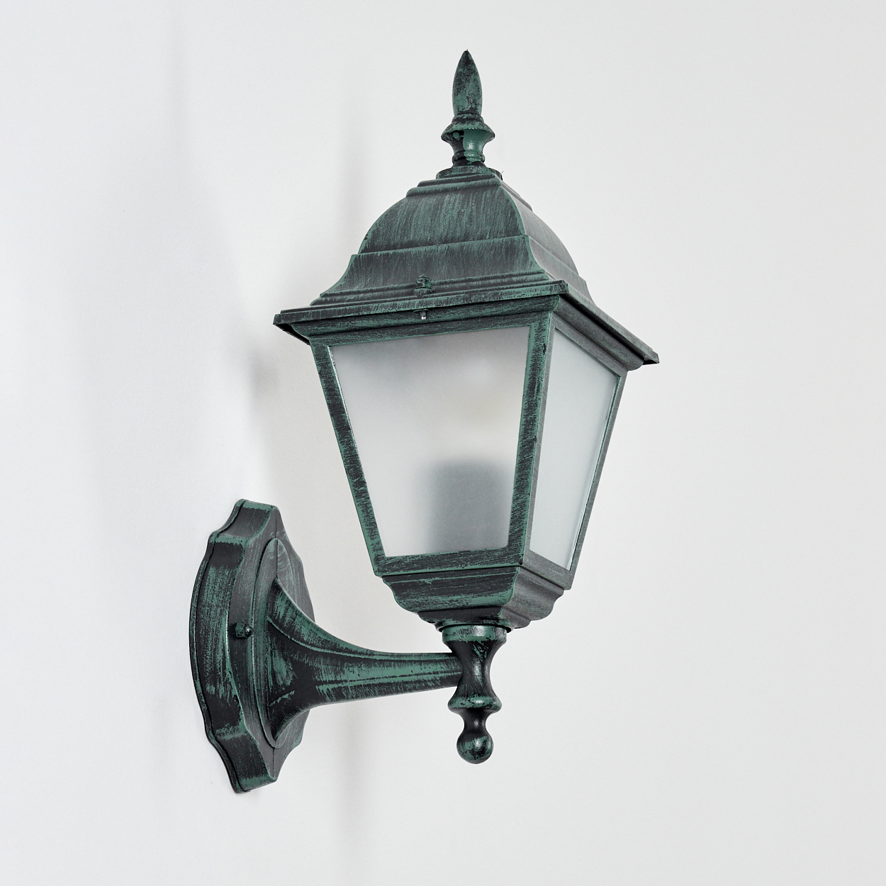 Grüne Außenwandleuchte. An einer weißen Wand montiert. Mattiertes Glas und ein dekoratives Oberteil. Die Lampe ist aus.