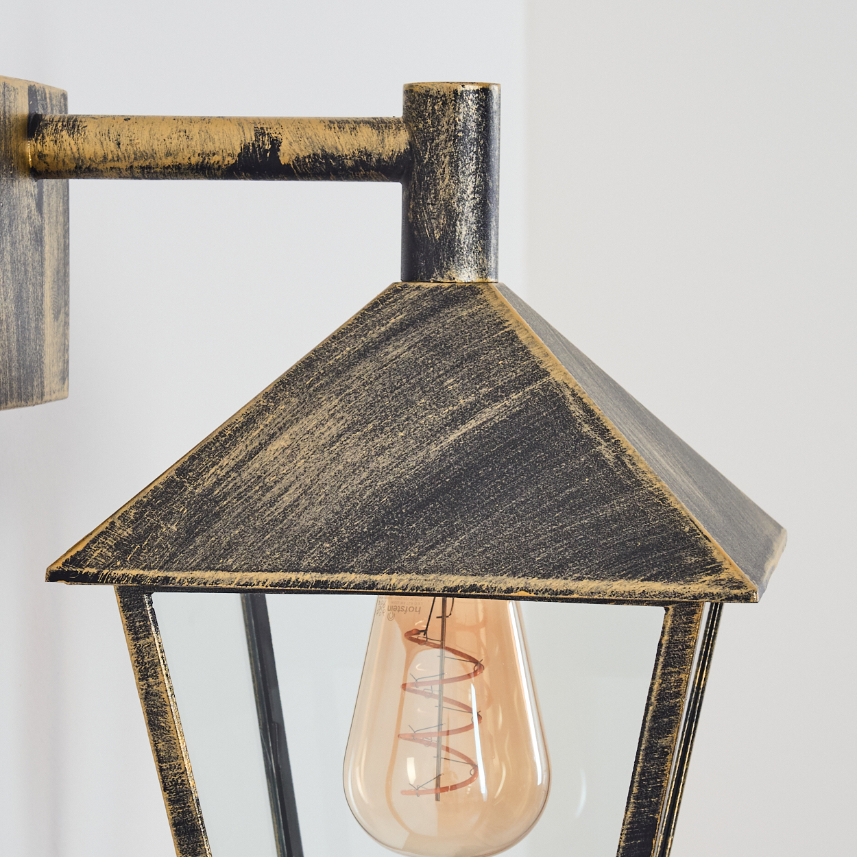 Nahaufnahme einer Vintage-Wandlampe. Sie hat eine schwarz-goldene Oberfläche und ist an einer weißen Wand befestigt.