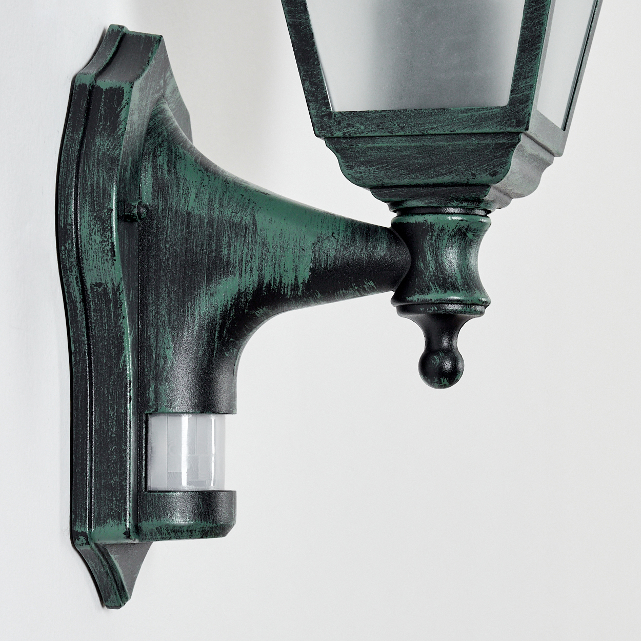 Eine grüne Vintage-Wandlampe mit Sensor. Die Lampe ist an einer weißen Wand befestigt. Die Oberfläche ist abgenutzt.