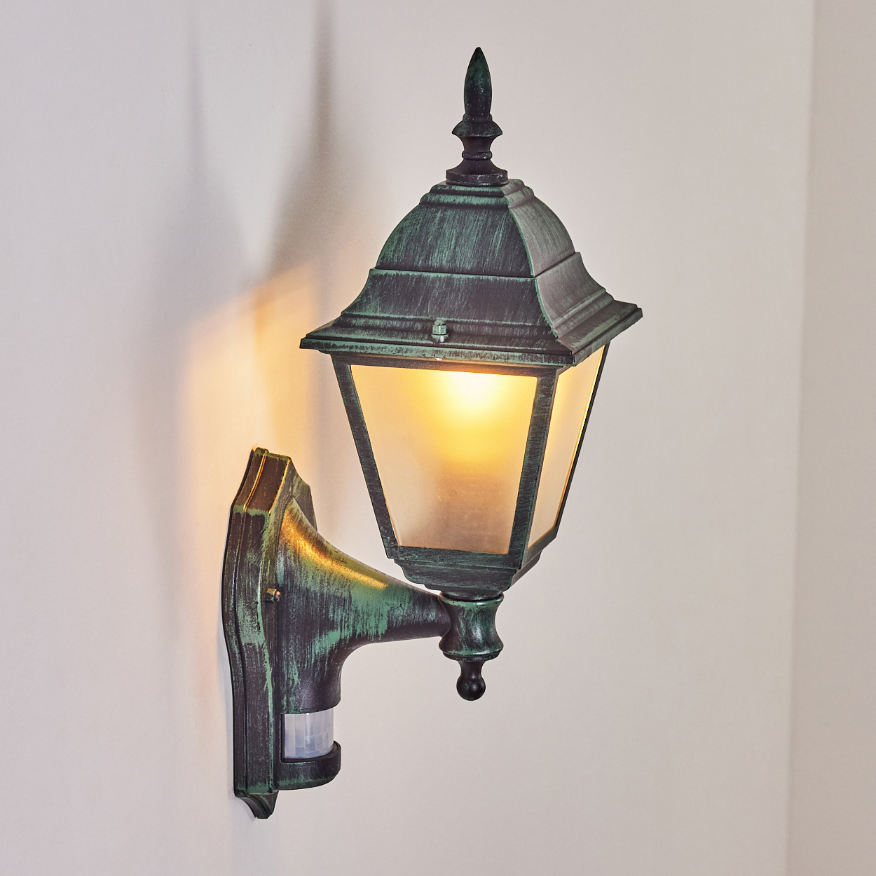Grüne Außenlampe an der Wand, mit leuchtender Glühbirne und Bewegungssensor.