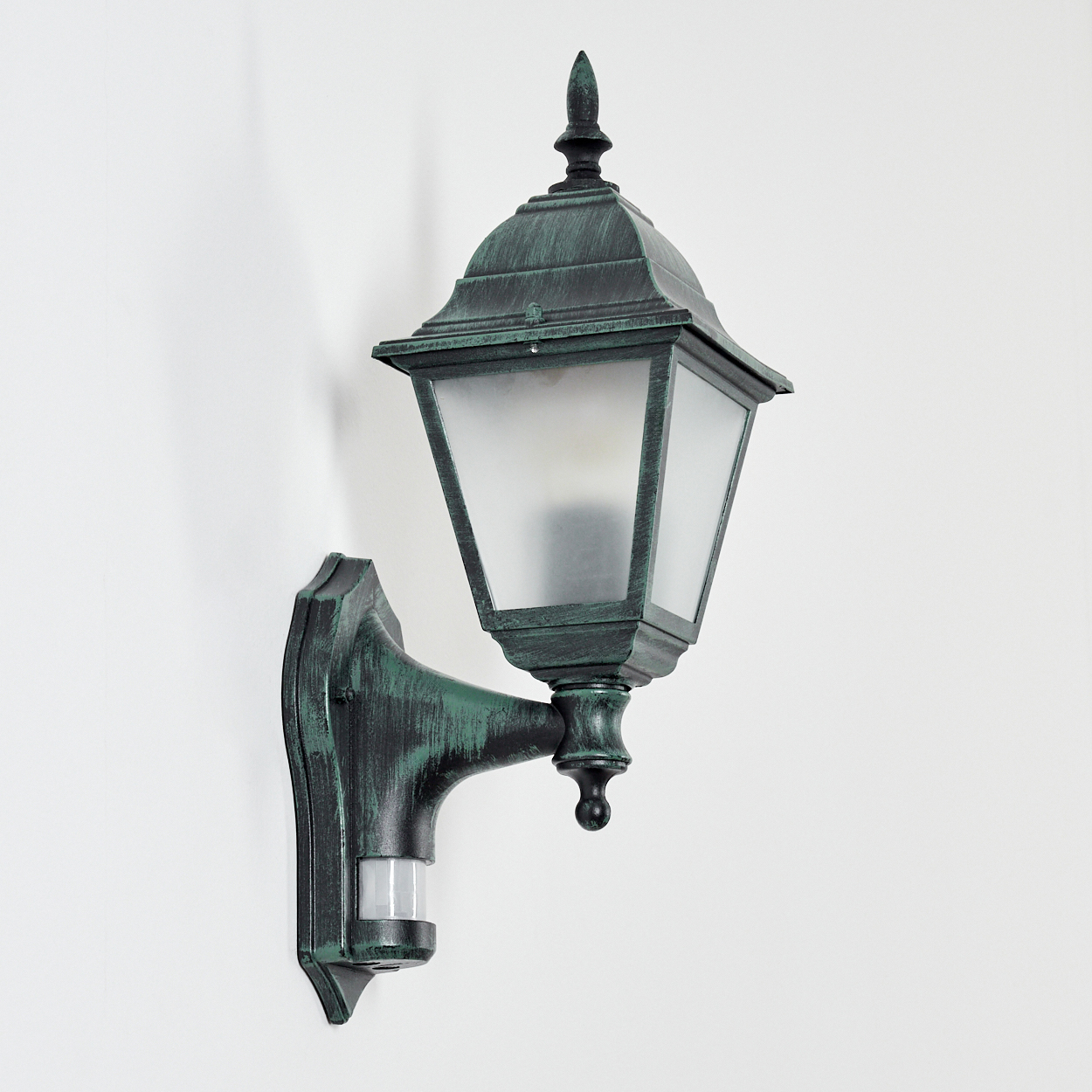 Grüne Außenlampe an der Wand, zeigt eine mattierte Glühbirne und einen Bewegungssensor.