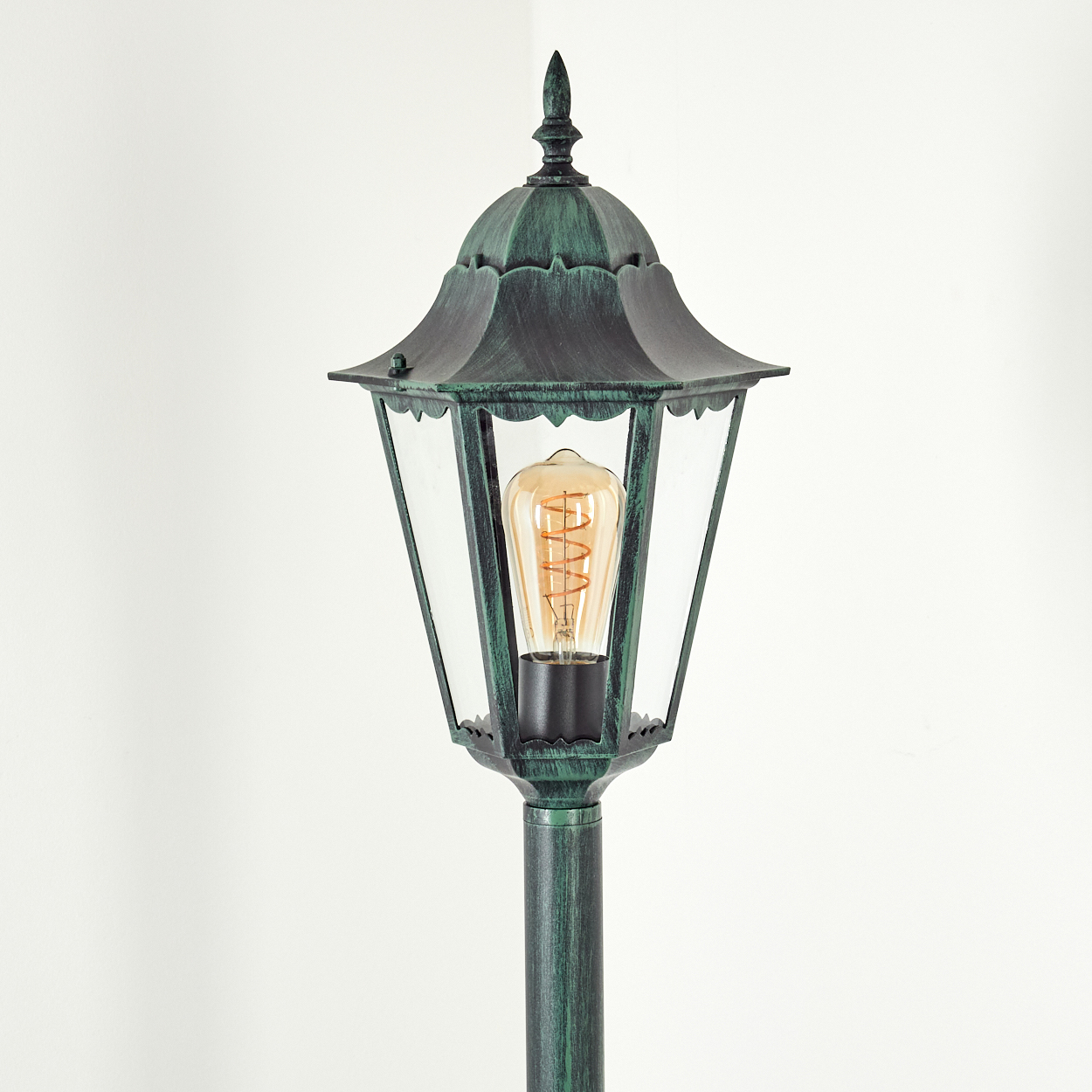 Grüne Außenlampe mit leuchtender Glühbirne, vor weißem Hintergrund, zeigt Lampendetails.